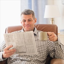 Man sitting in living room with newspaper and mug. Photo : Daniel Grill