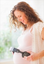 Portrait of pregnant woman holding headphones on her belly. Photo : Daniel Grill