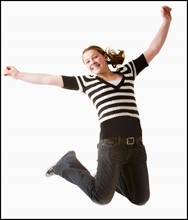 Studio shot of girl (12-13) jumping with arms raised. Photo : Mike Kemp