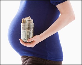 Studio Shot of mid section of pregnant woman holing jar with money. Photo : Mike Kemp