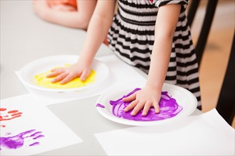 Girl (4-5) holding her hands on plates with paint. Photo : Mike Kemp