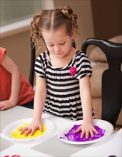 Girl (4-5) holding her hands on plates with paint. Photo : Mike Kemp