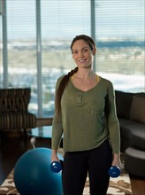 Portrait of mid adult woman exercising at home with dumbbells. Photo : Dan Bannister