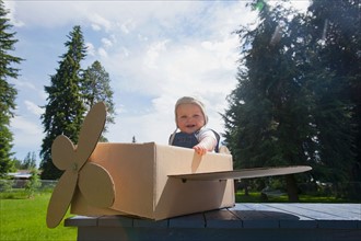 Baby boy (12-17 months) playing inside paper aeroplane made of cardboard box . Photo : Noah Clayton