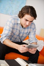 Young man sitting on sofa and using digital tablet. Photo : Rob Lewine