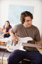 Young man playing electric guitar, young woman in background. Photo : Rob Lewine