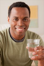 Portrait of smiling man holding glass of water. Photo : Rob Lewine