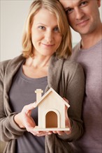 Mid adult couple holding wooden model of house. Photo : Rob Lewine