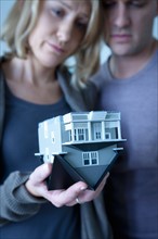 Mid adult couple holding wooden model of house. Photo : Rob Lewine
