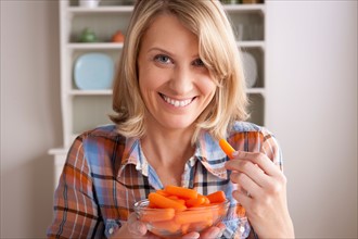 Portrait of mid adult woman with bowl of carrots. Photo : Rob Lewine