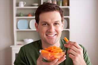 Portrait of mid adult man with bowl of carrots. Photo : Rob Lewine