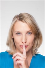 Studio shot of mid adult woman with finger on lips. Photo : Rob Lewine