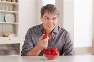 Portrait of mature man with strawberries on table. Photo : Rob Lewine