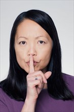 Studio portrait of mature woman with finger on lips. Photo : Rob Lewine