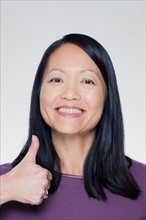 Studio portrait of mature woman showing thumbs up sign. Photo : Rob Lewine