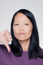 Studio portrait of mature woman showing thumbs down sign. Photo : Rob Lewine