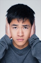 Studio portrait of young man covering ears. Photo : Rob Lewine