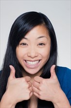 Studio portrait of young woman showing thumbs up sign. Photo : Rob Lewine