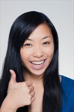 Studio portrait of young woman showing thumbs up sign. Photo : Rob Lewine