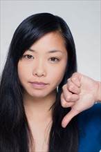 Studio portrait of young woman showing thumbs down sign. Photo : Rob Lewine