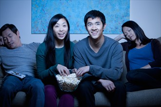 Smiling family watching TV and eating popcorn. Photo : Rob Lewine