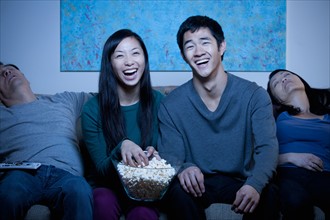 Smiling family watching TV and eating popcorn. Photo : Rob Lewine