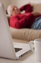 Senior man sleeping on sofa, laptop and mug in foreground. Photo : Rob Lewine