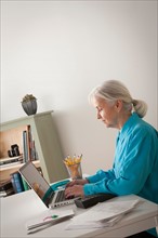 Senior woman working on laptop in home office. Photo : Rob Lewine