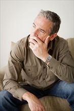 Worried mature man sitting on sofa. Photo : Rob Lewine