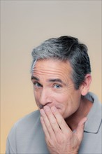 Studio Portrait of mature man covering mouth with hand. Photo : Rob Lewine