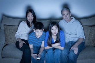 Family sitting on sofa and watching television. Photo : Rob Lewine