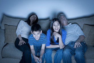 Family sitting on sofa and watching television. Photo : Rob Lewine
