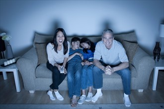 Family sitting on sofa and watching television. Photo : Rob Lewine