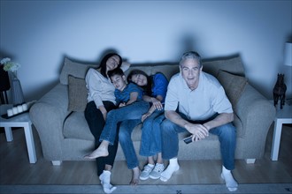 Family sitting on sofa and watching television. Photo : Rob Lewine