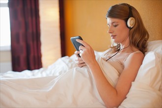 Young pregnant woman listening to music in bed. Photo : Mark de Leeuw