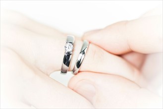 Close-up studio shot of man's hand putting wedding ring next to engagement ring on female hand .