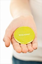 Close-up studio shot female hand holding yellow volunteer badge. Photo : Elena Elisseeva