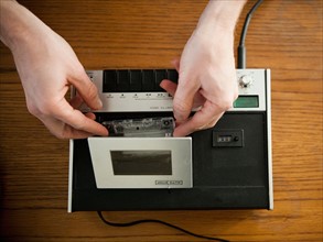 Close-up view of human hands putting tape into old-fashioned tape recorder. Photo : Jessica