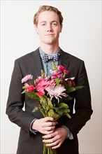 Portrait of young handsome man holding bunch of flowers. Photo : Jessica Peterson