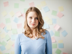 Indoor portrait of young attractive woman standing in f front of wall covered in adhesive notes.