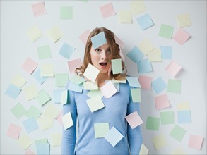 Indoor portrait of young attractive woman standing in f front of wall covered in adhesive notes.