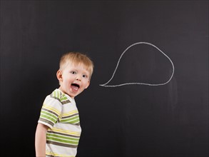 Studio portrait of happy toddler boy (2-3) with blank speech bubble written on blackboard. Photo :
