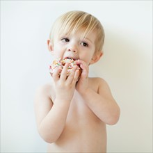 Studio portrait of cute toddler boy (2-3) eating doughnut. Photo : Jessica Peterson
