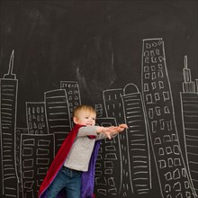 Cute toddler boy (2-3) standing against blackboard with city skyline drawn on it. Photo : Jessica