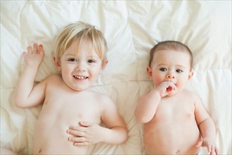 Toddler boy (2-3) lying in bed with baby sister (6-11 months). Photo : Jessica Peterson