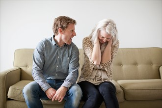 Young couple arguing while sitting on sofa. Photo : Jessica Peterson