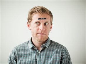 Studio shot of young man with black concept label on forehead. Photo : Jessica Peterson