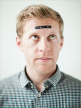 Studio shot of young man with black concept label on forehead. Photo : Jessica Peterson