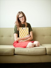 Young woman sitting on sofa with clipboard. Photo : Jessica Peterson
