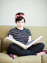 Young woman sitting on sofa with book. Photo : Jessica Peterson